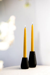 2 black charred wooden candlesticks on a cream tablecloth with yellow beeswax candles in them, lit