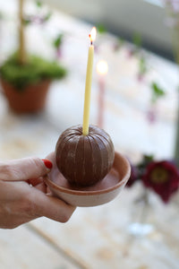 A small chocolate egg placed on a terracotta dish with a single celebration beeswax candle liit in it