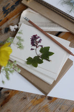 Load image into Gallery viewer, An image of 5 cream cards laid ontop of brown kraft envelopes with a pencil and presses purple blue bell on top
