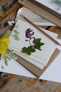 An image of 5 cream cards laid ontop of brown kraft envelopes with a pencil and presses purple blue bell on top