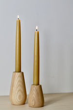 Load image into Gallery viewer, A pair of wood turned candlestick holders each with a natural beeswax dinner candles in. two different sizes showed, one small and one medium. Beautiful curved shape of the simple holder shows off the natural wood grain.
